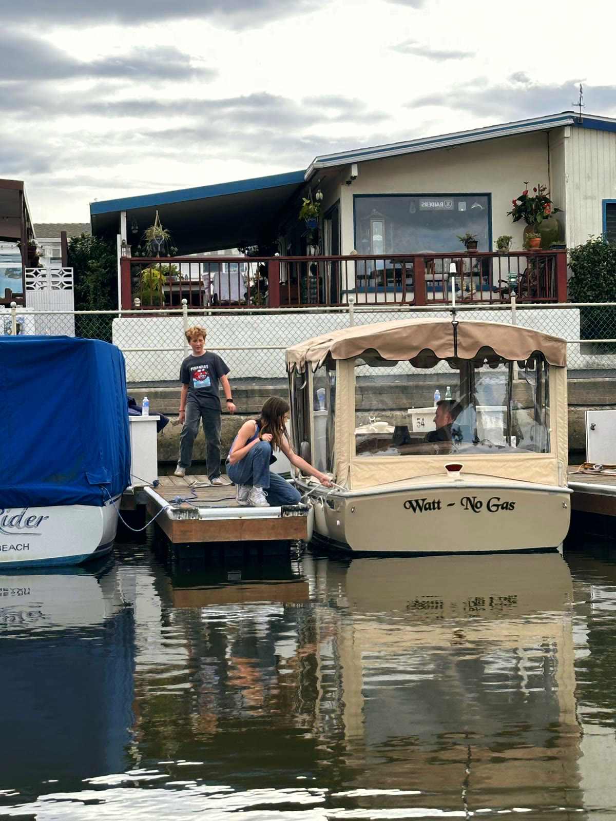 Two kids on a dock finger loading up a Duffy electric boat at Bayside Village Marina, with a village home and deck behind