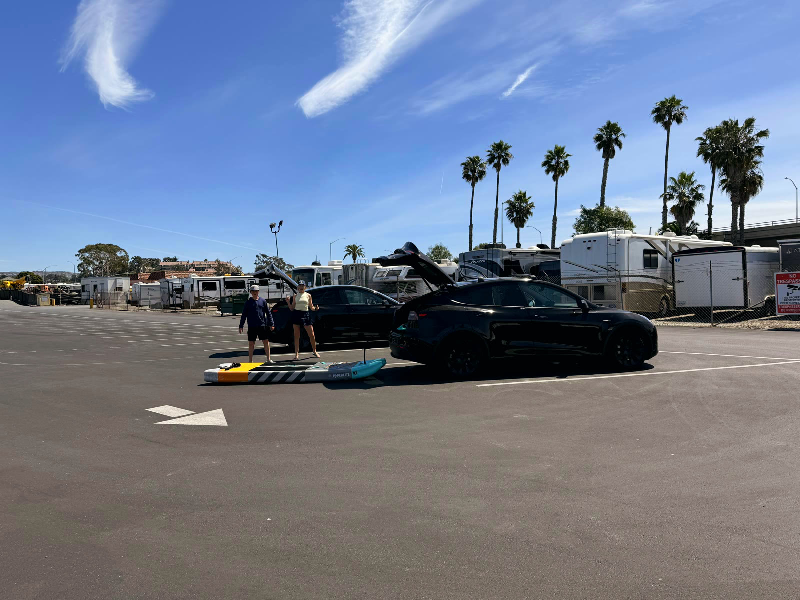 The Bayside Village Marina tenant parking lot with palms and the RV storage rows behind, a paddleboard coming out of a car trunk