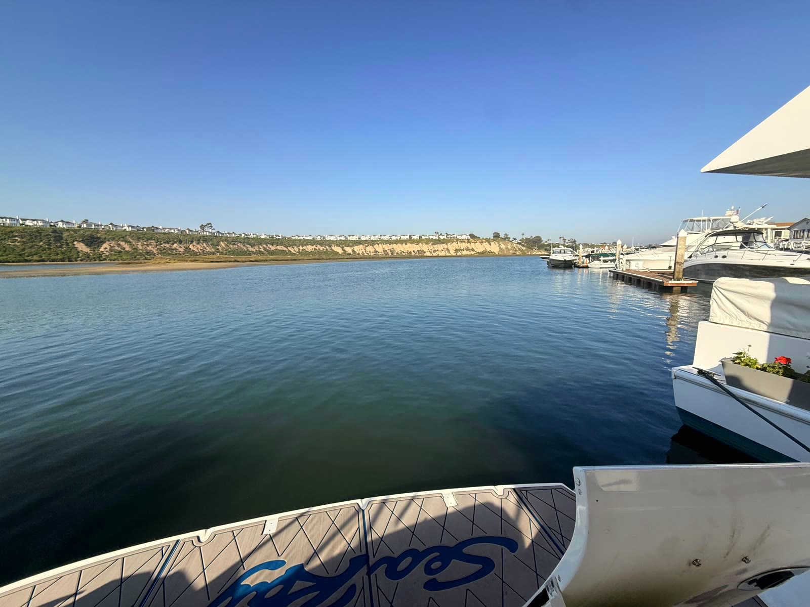The view from a Bayside Village slip across glassy Upper Newport Bay water toward the bluffs and homes of Dover Shores