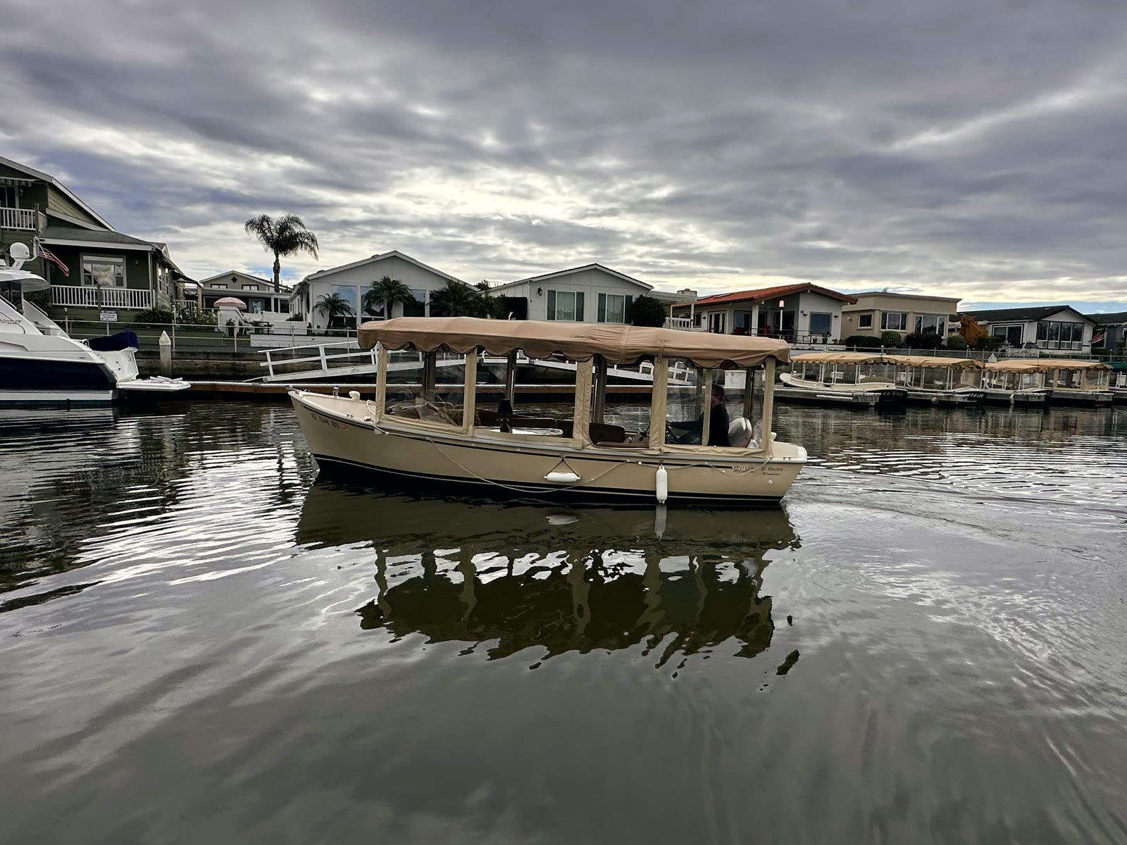A Duffy electric boat idling along the Bayside Village channel in front of the village's waterfront homes under a moody sky
