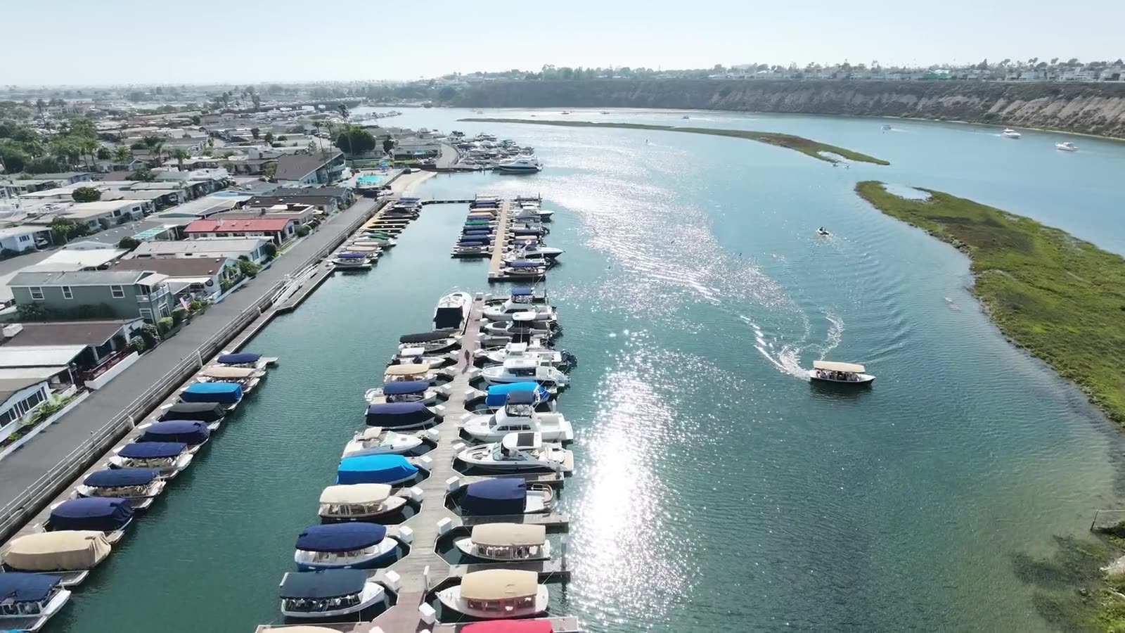 Drone flight down the sparkling Back Bay channel past the Bayside Village docks, toward the bluffs of Upper Newport Bay