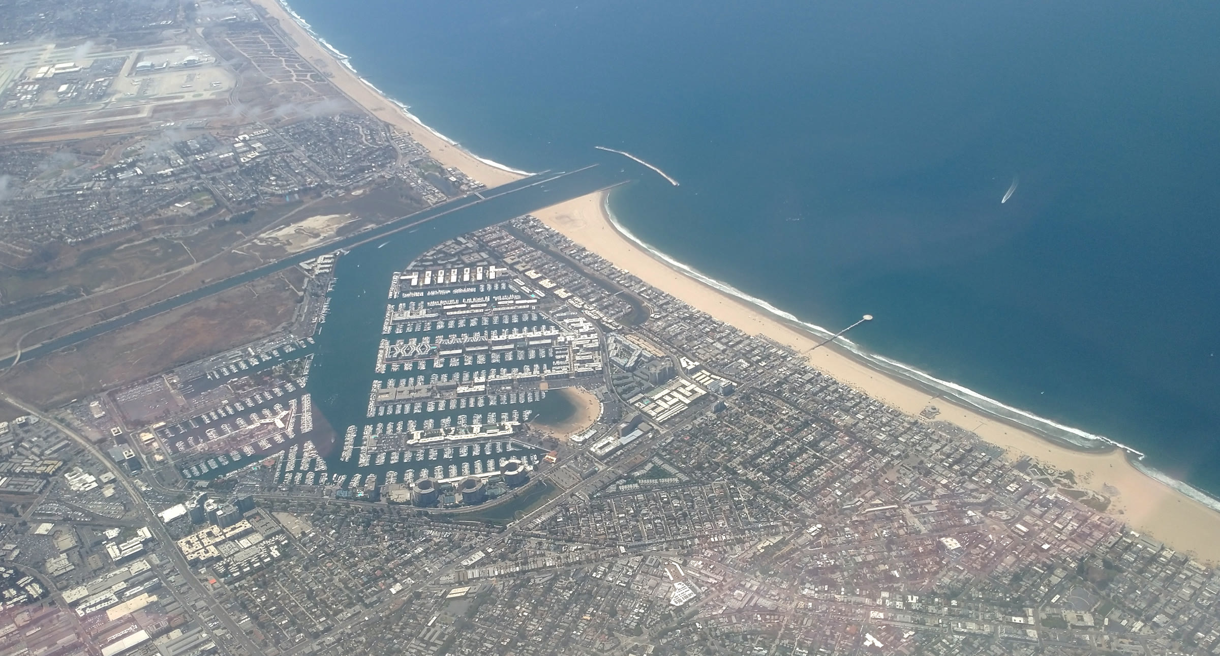 Aerial view of Marina del Rey — the eight lettered basins and main channel meeting Santa Monica Bay behind the detached breakwater, with Venice Beach stretching up the coast