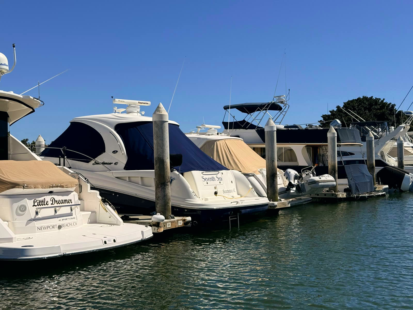 Boats stern-to along a Newport Dunes Marina dock on a clear blue day, dock pilings and power pedestals in the foreground