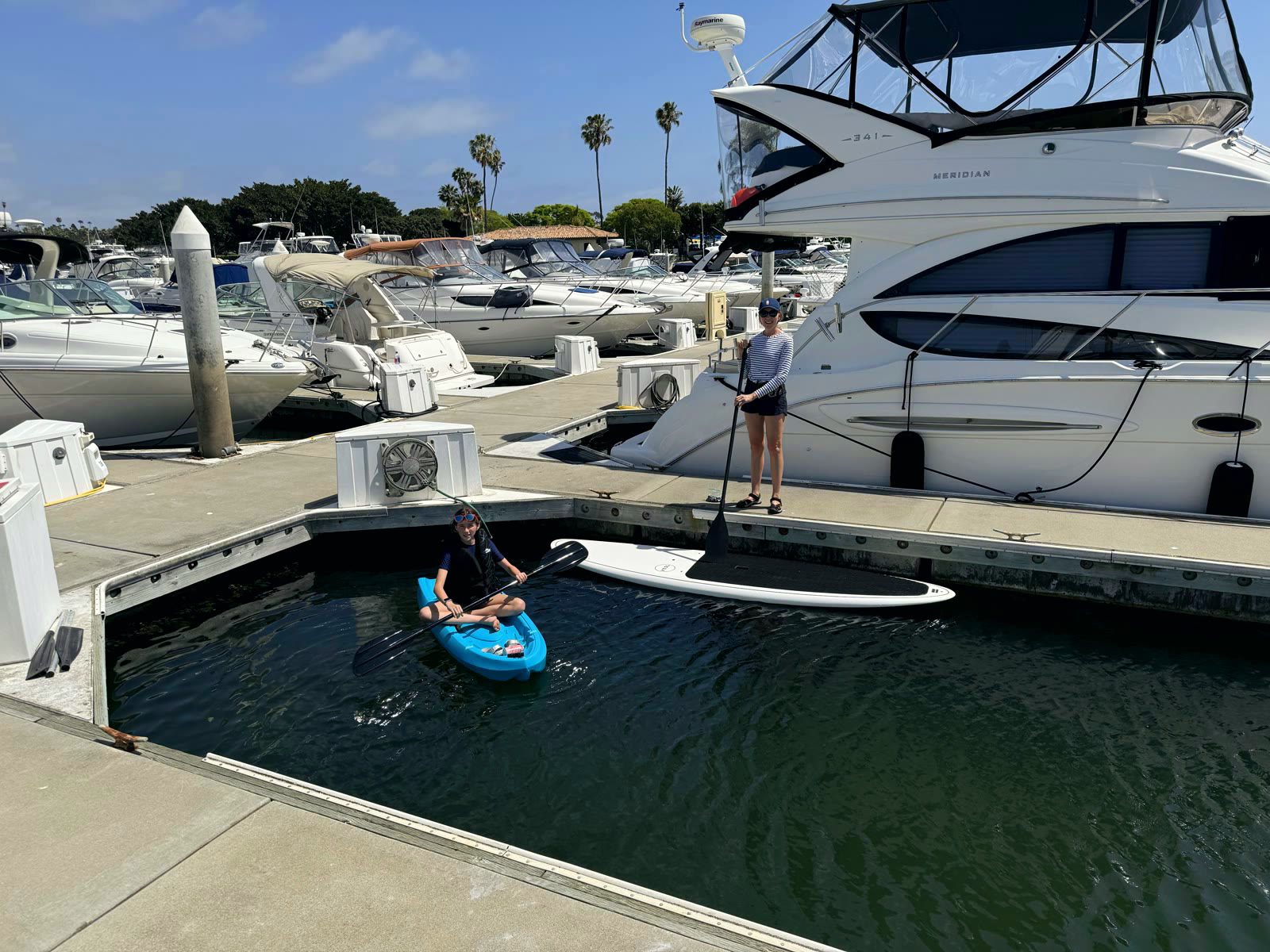 A paddleboarder and a kid in a kayak launching right from a Newport Dunes Marina slip between the docks
