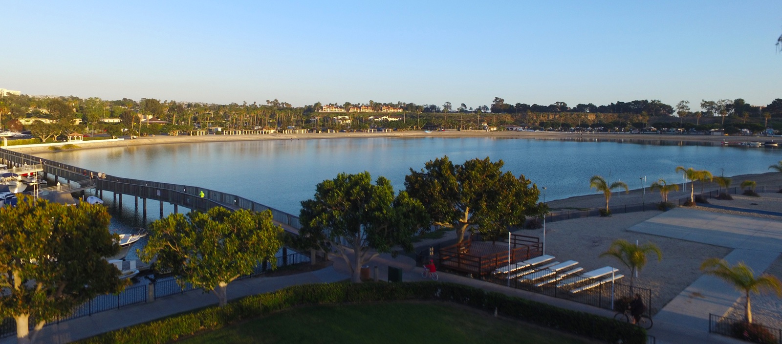 The Newport Dunes swim lagoon at golden hour — the beach, the arcing footbridge over the lagoon entrance, and marina docks at the left